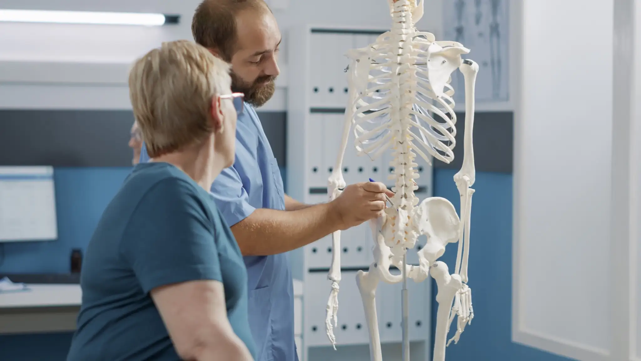 male doctor pointing human skeleton show spinal cord explain mechanical disorders rehabilitation cabinet specialist explaining back bones system physical therapy scaled